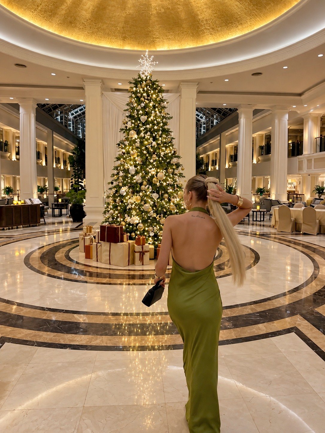Model in an olive satin dress walking toward a Christmas tree in a grand hotel lobby