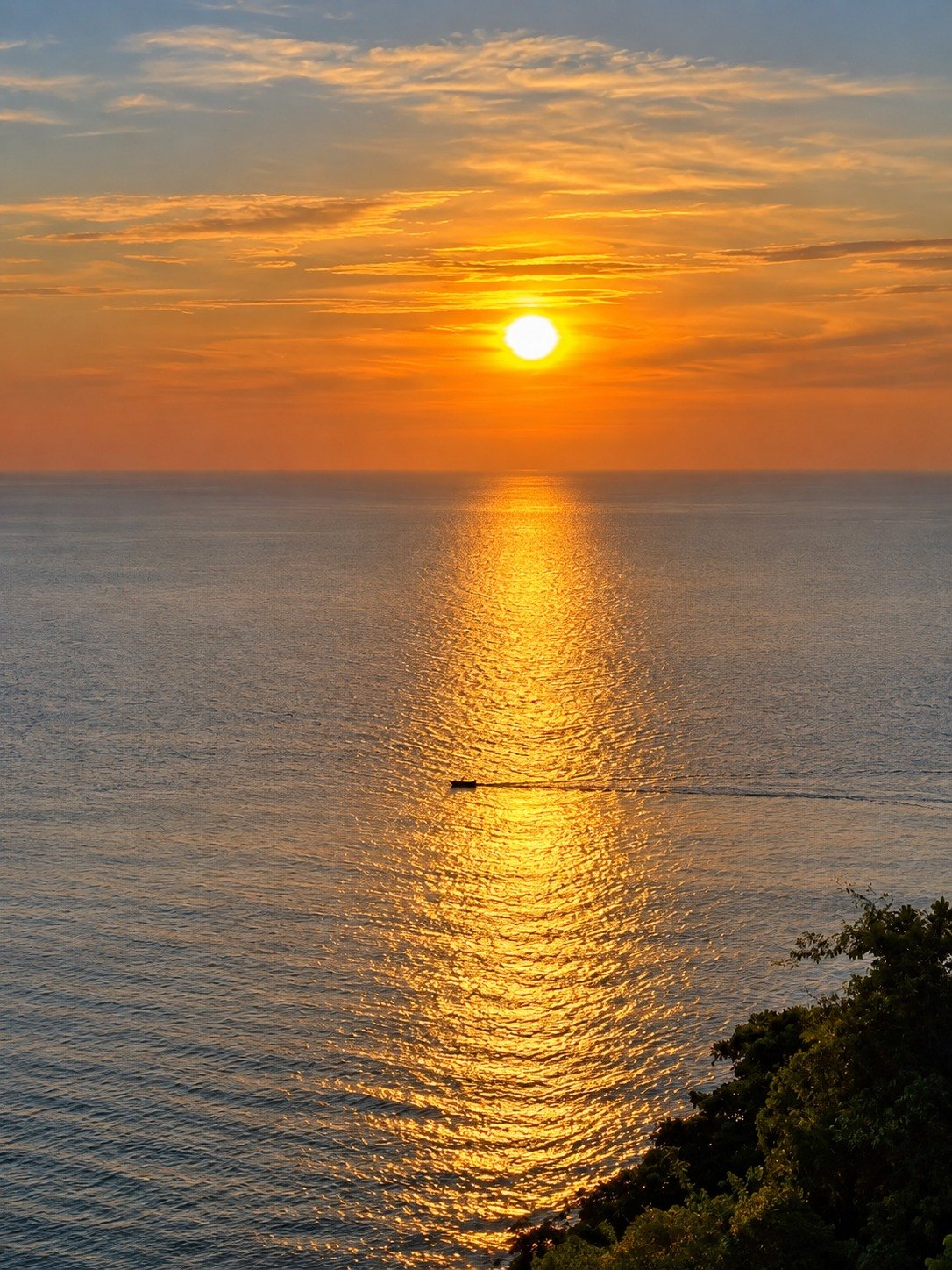 Sun setting over the sea with a lone boat, seen from a Thai island
