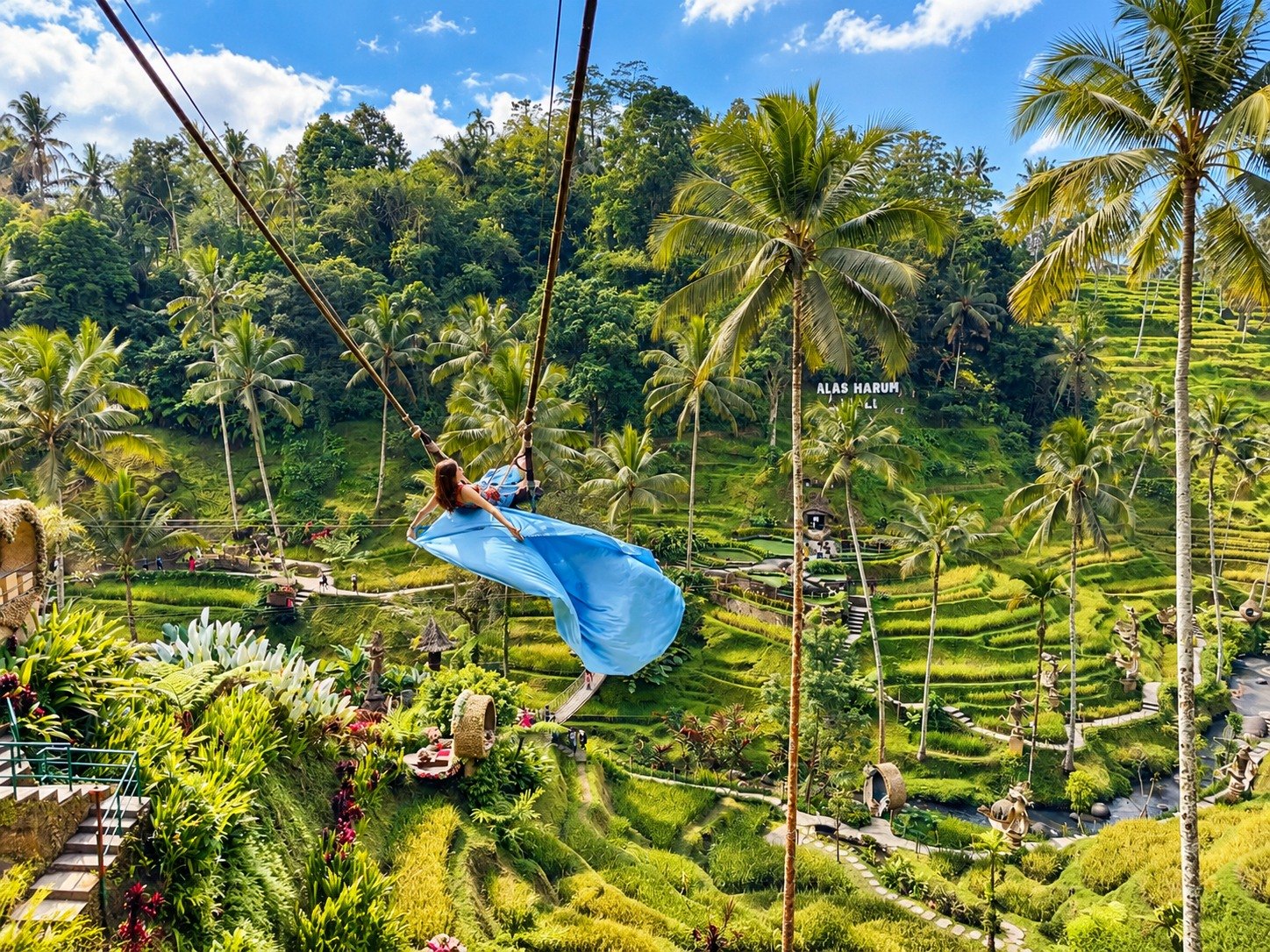 Woman in a flowing blue dress on a jungle swing above Bali's rice terraces
